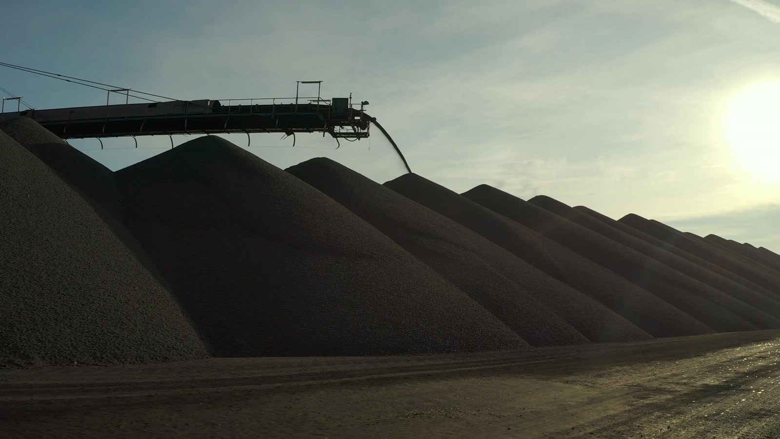 Iron ore stockpiles beside a stacker conveyor.